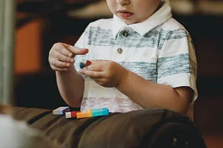Kleines Kind in gestreiftem Poloshirt spielt mit bunten Legosteinen auf einem Kissen.