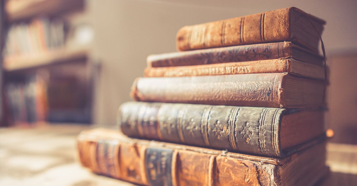 Auf einem Holztisch liegt ein Stapel alter Bücher. Die Einbände sind altersbedingt teils beschädigt, die Titel der Bücher sind nicht leserlich.