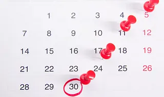 Kalenderblatt mit roten Stecknadeln an mehreren Tagen und dem 30. Tag, der rot eingekreist ist.