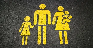 Gelbes Piktogramm einer Familie mit Vater, Mutter mit Baby und Kind auf Asphalt gemalt.