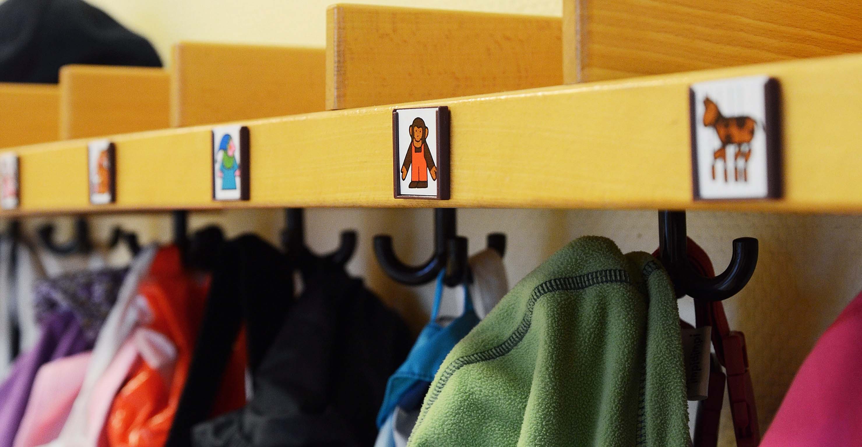 Kindergarderobe mit bunten Jacken an Haken und Piktogrammen über jedem Haken.