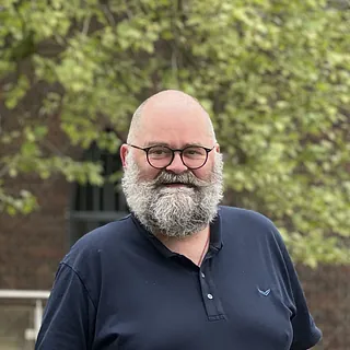 Portrait von Peik Otto, lächelnd vor einem Baum und Geländer im Freien.