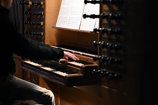 Eine Person spielt Orgel mit sichtbaren Registerzügen und Notenblatt.