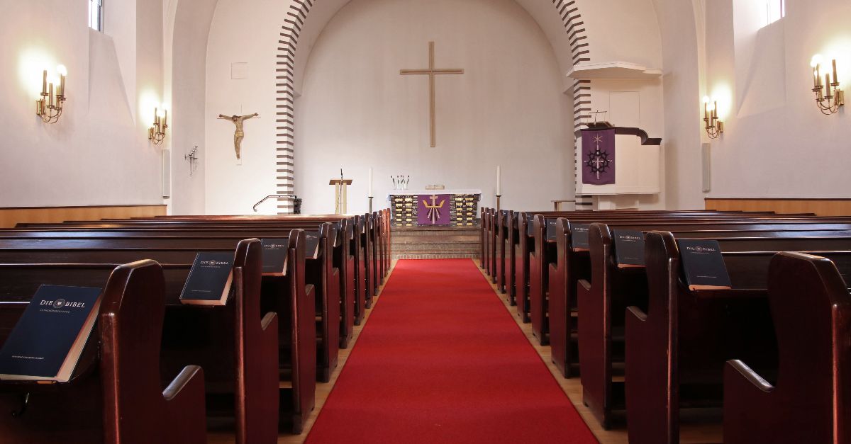 Innenraum der Adolf-Clarenbach-Kirche mit roten Teppichgang, Holzbänken und Altar mit Kreuz an der Wand.