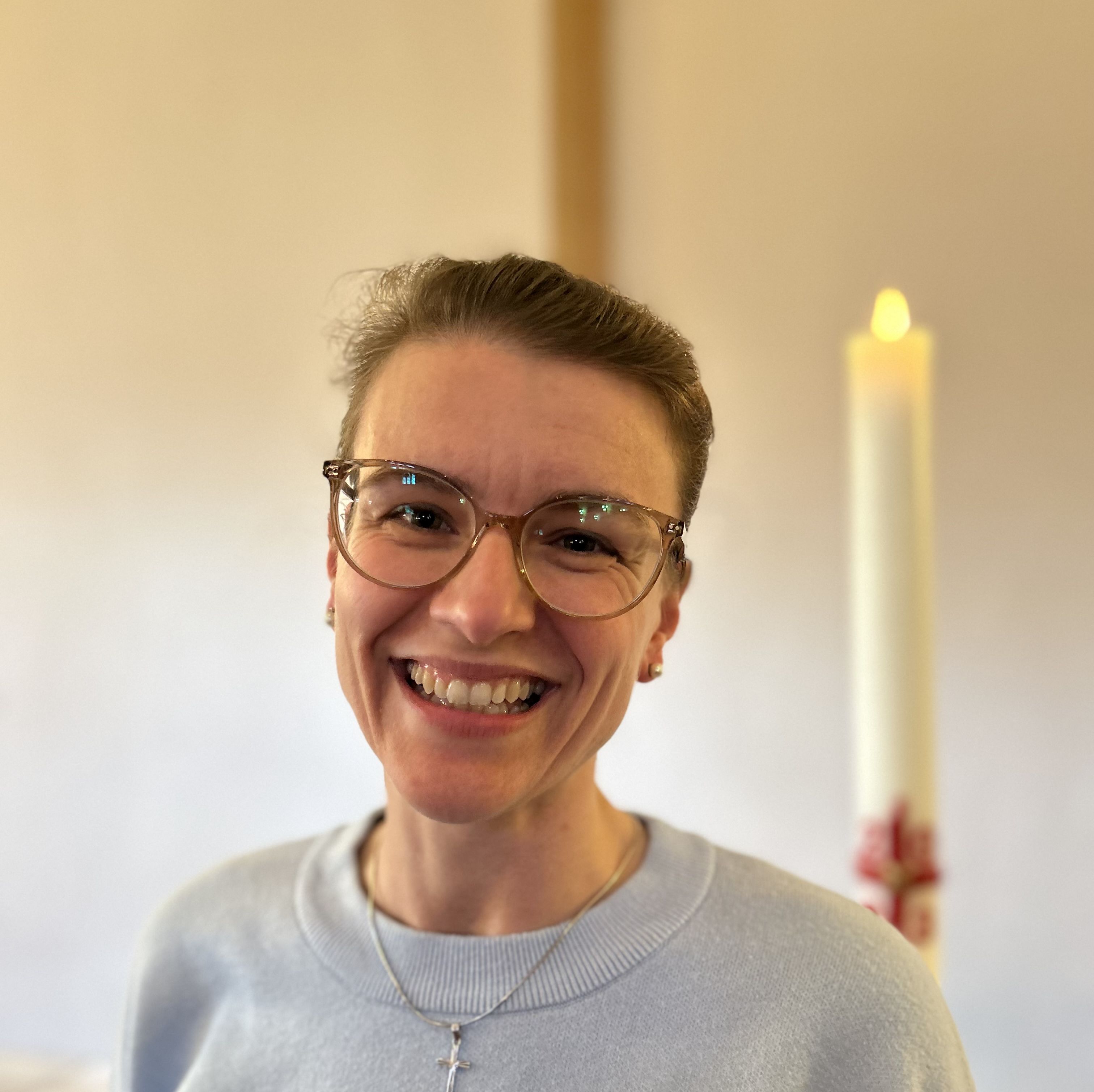 Portrait von Anja vom Bruch, lächelnd und mit Kreuzkette vor einer brennenden Kerze.