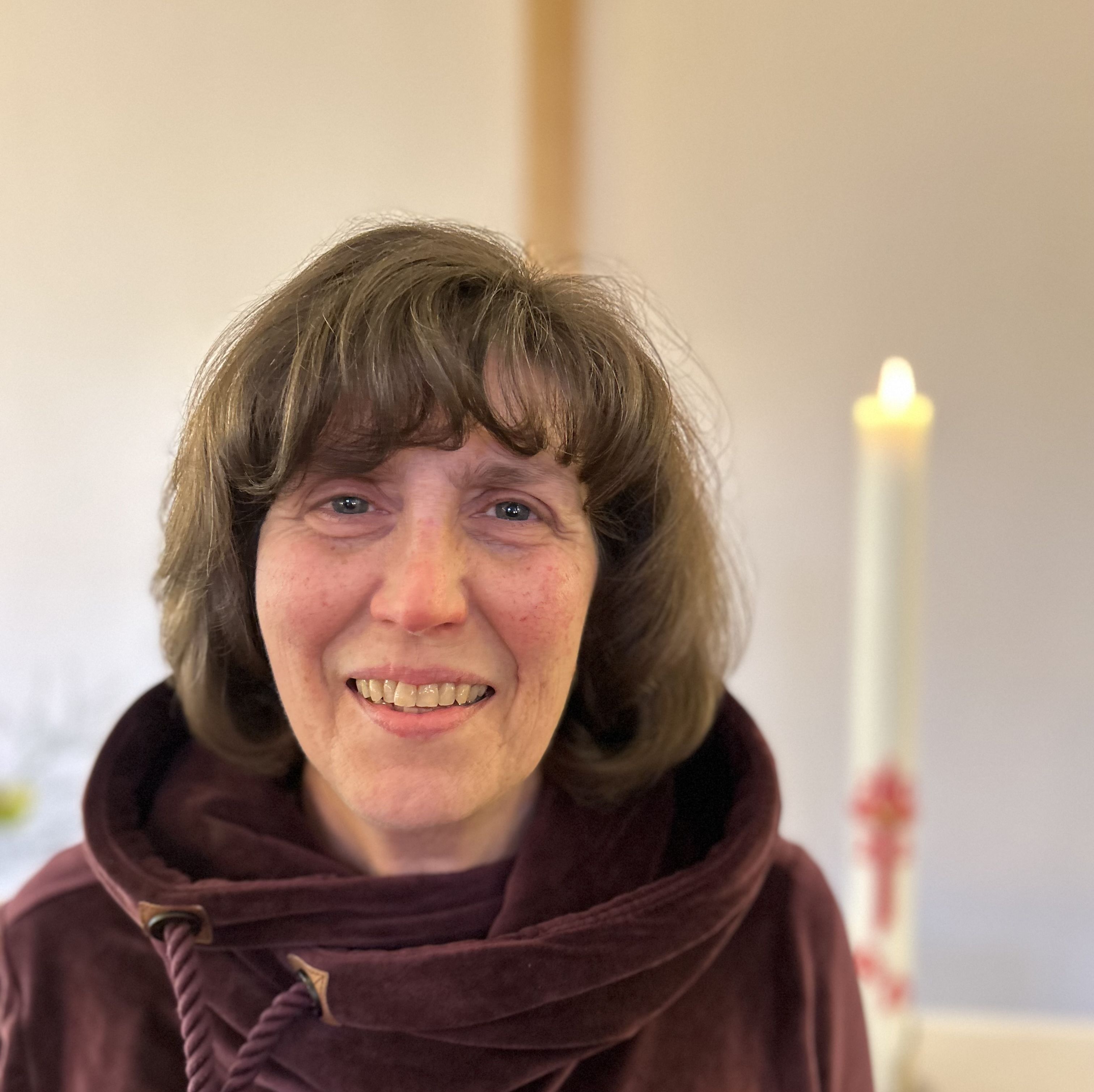 Portrait von Susanne Werntges, lächelnd, vor unscharfem Hintergrund mit Kerze und Blumen.