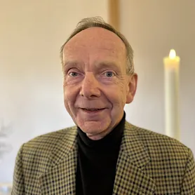 Portrait von Tilo Breyer im kariertem Sakko und schwarzem Rollkragenpullover, lächelnd vor einer brennenden Kerze.