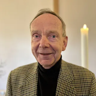 Portrait von Tilo Breyer im kariertem Sakko und schwarzem Rollkragenpullover, lächelnd vor einer brennenden Kerze.