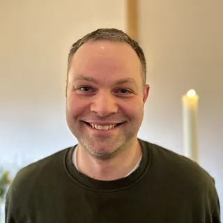 Portrait von Thomas Bammert vor unscharfem Hintergrund mit Kerze und Blumen