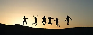 Eine Gruppe Jugendlicher springt in die Luft vor einem Abendhimmel.