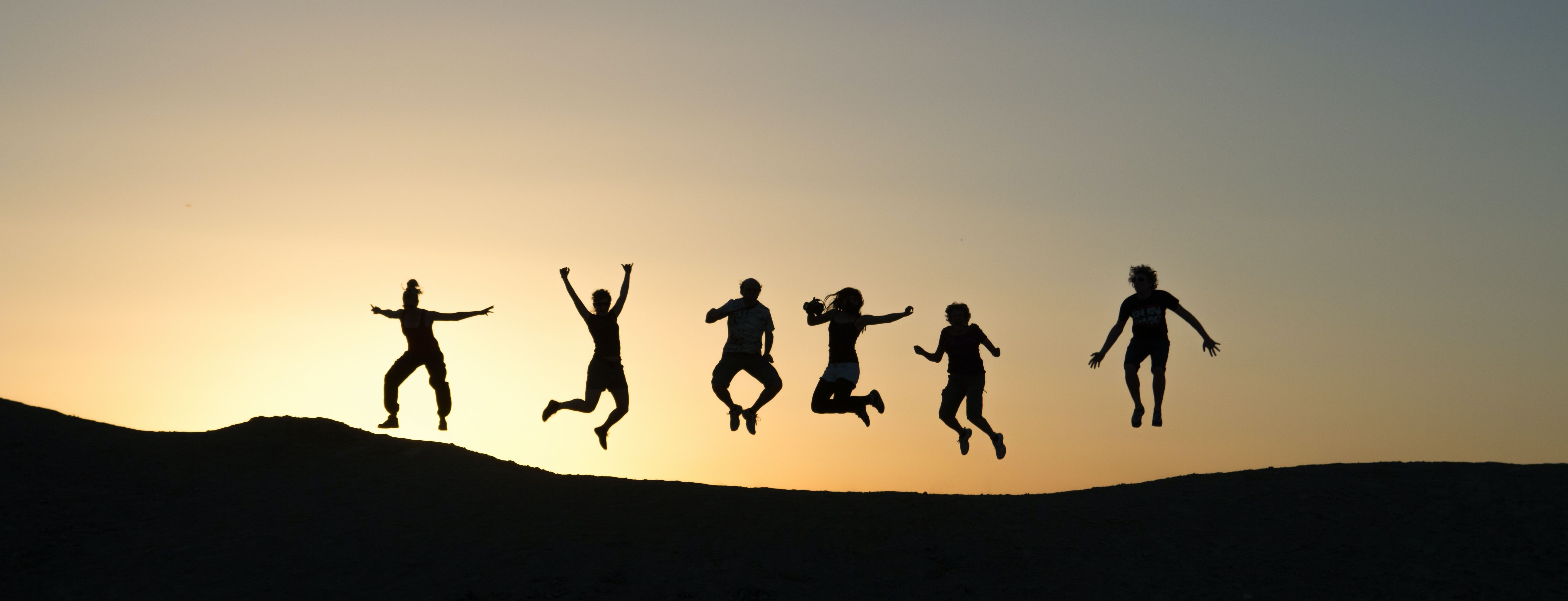 Eine Gruppe Jugendlicher springt in die Luft vor einem Abendhimmel.