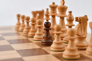 Schachbrett mit einer Reihe von weißen Figuren und einem einzelnen schwarzen Bauern in der Mitte.