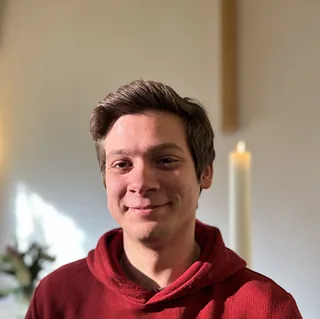 Portrait von Marko Schellmat, lächelt vor einem weißen Hintergrund mit einer brennenden Kerze.