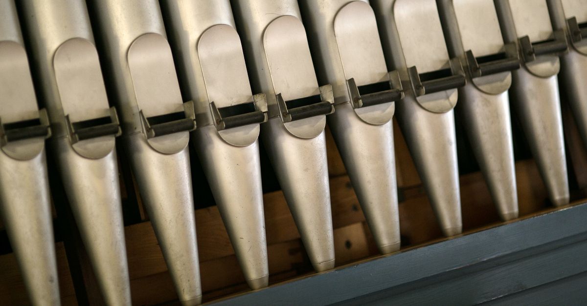 Nahaufnahme von vertikal angeordneten Metallpfeifen einer Orgel mit Öffnungen am unteren Ende.