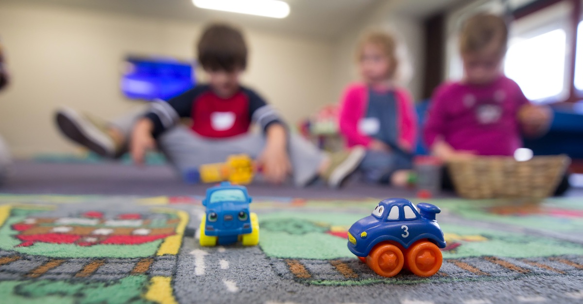 Spielzeugautos auf einer Spielmatte mit Straßen, im Hintergrund sitzen drei Kinder unscharf auf dem Boden.