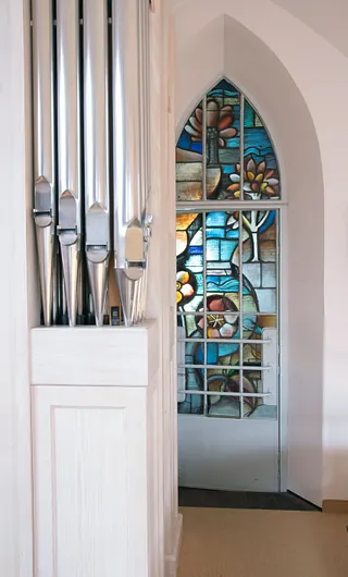 Orgelpfeifen neben einem spitzbogigen Buntglasfenster mit Blumenmotiven in der Adolf-Clarenbach-Kirche.