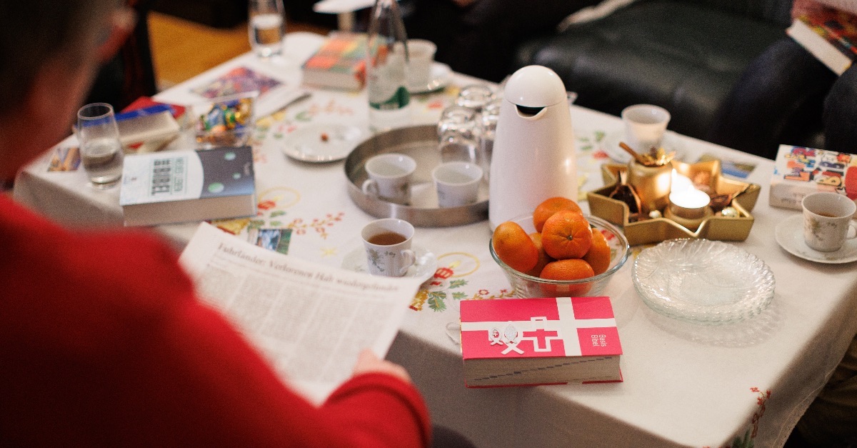 Um einen gedeckten Wohnzimmertisch sitzen Menschen, miteinander im Gespräch. Auf dem Tisch liegen Bibeln, Orangen, stehen Wassergläser, Kaffee- und Teetassen.