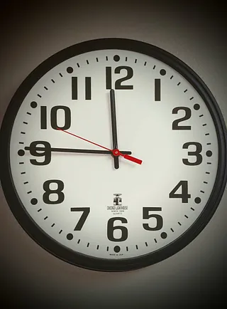 Eine runde Wanduhr mit schwarzem Rahmen zeigt 11:45:48 Uhr.