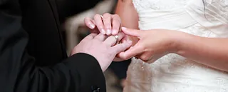 Eine Braut steckt dem Bräutigam einen Ehering an den Finger während der Trauung.