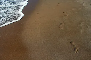 Fußspuren im Sand am Strand neben anbrandenden Wellen.