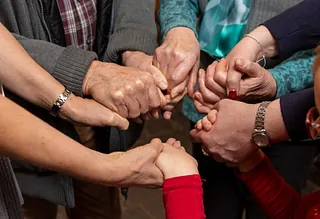 Mehrere Menschen halten sich an den Händen in einem Kreis, symbolisieren Zusammenhalt und Gemeinschaft.