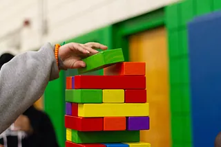 Eine Kinderhand legt einen Bauklotz auf einen Turm bunter Bauklötze.